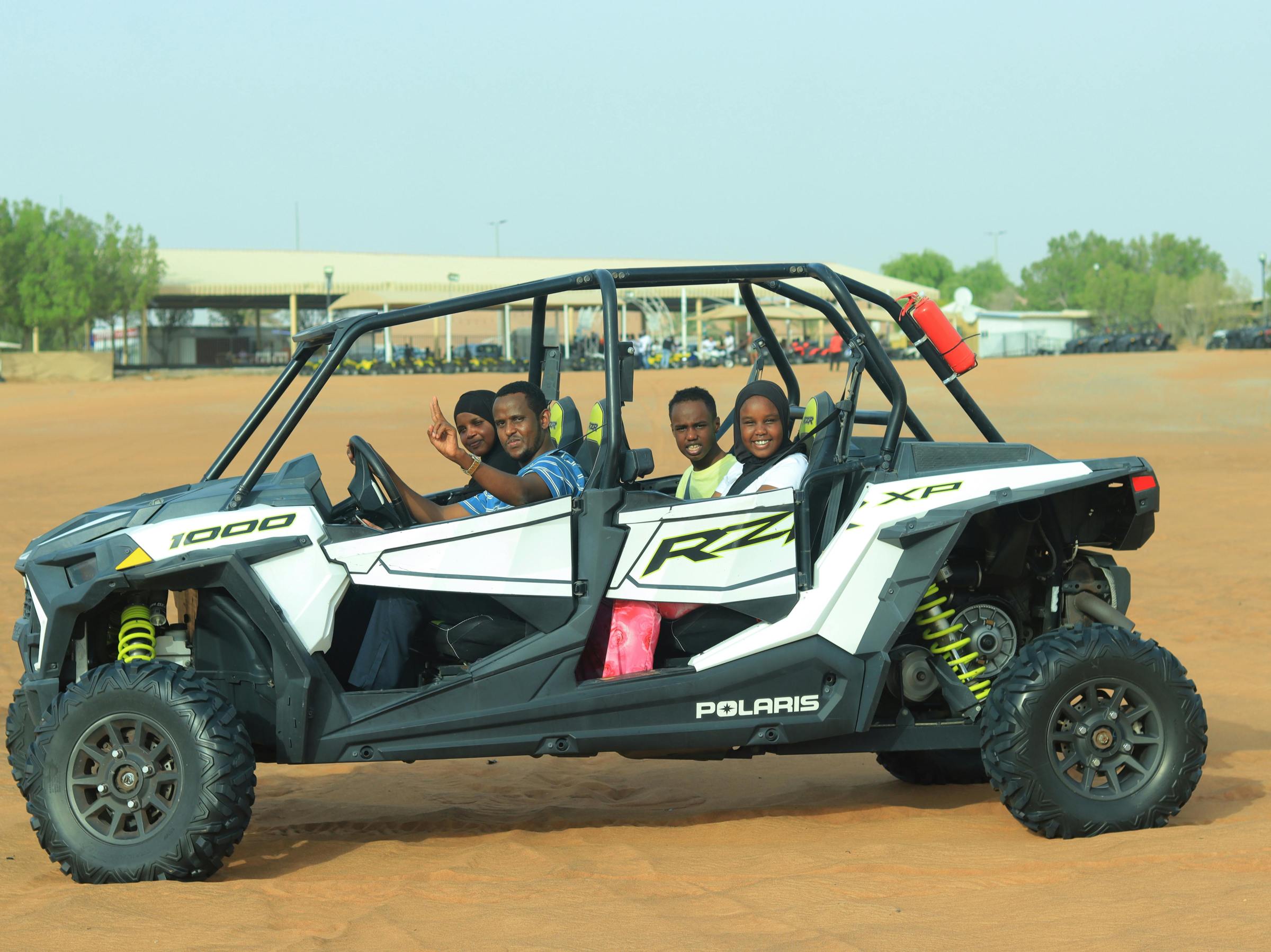 Four people sitting in an off-road vehicle on a sandy terrain.