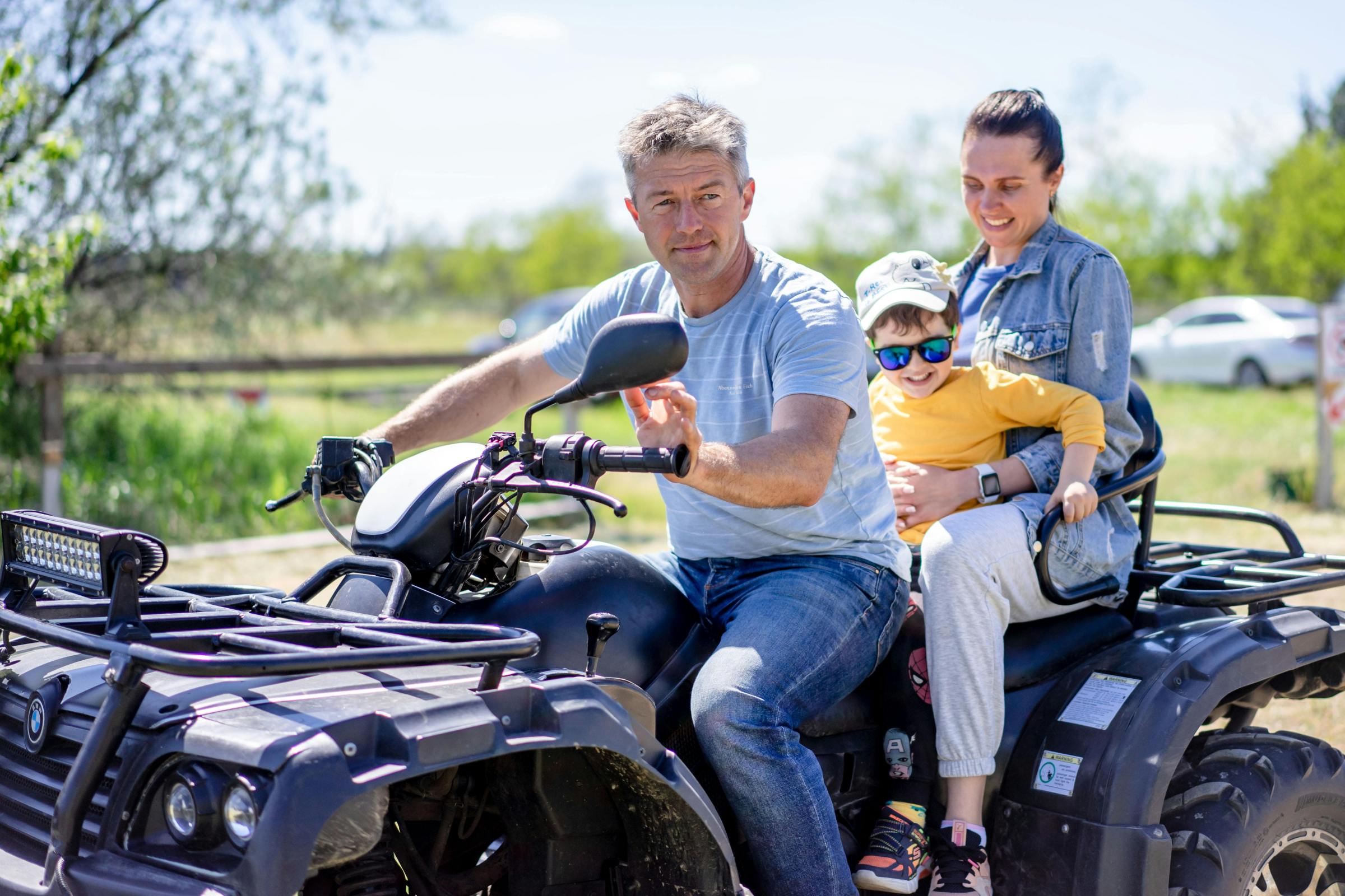 Family of three riding an ATV outdoors on a sunny day.