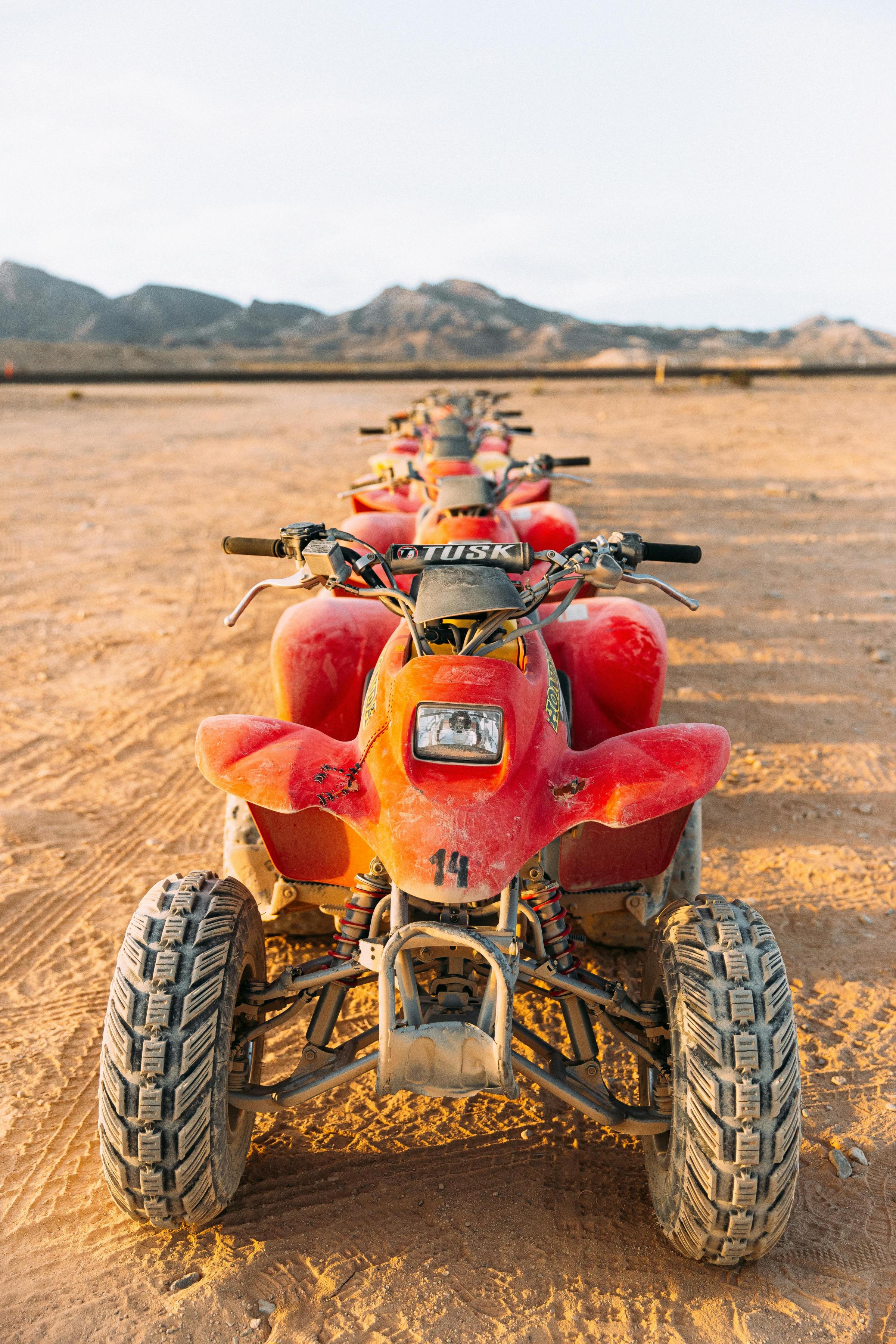 Row of red ATVs lined up on a dirt path with mountains in the background.