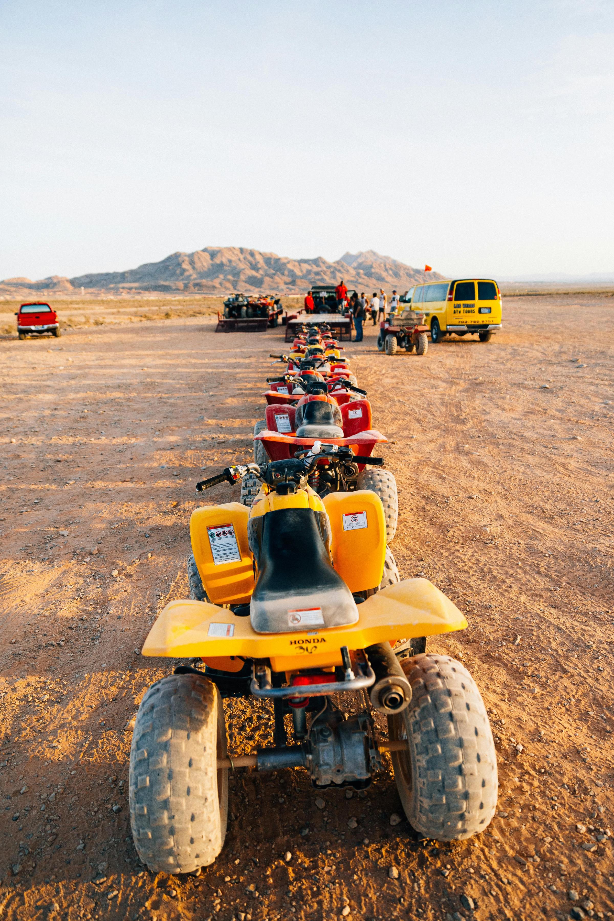 Line of ATVs on a desert terrain with mountains in the background under a clear sky.