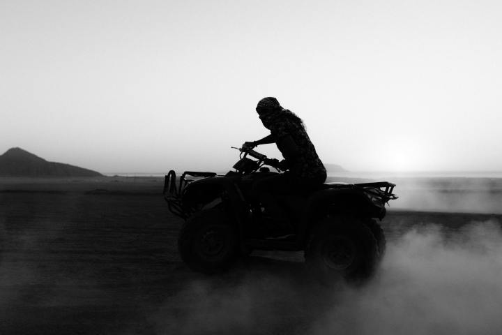 Silhouette of a person riding a quad bike on a dusty plain at dawn or dusk.