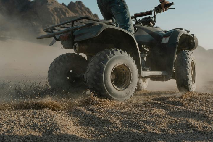 Person riding an ATV on sand with mountains in the background.